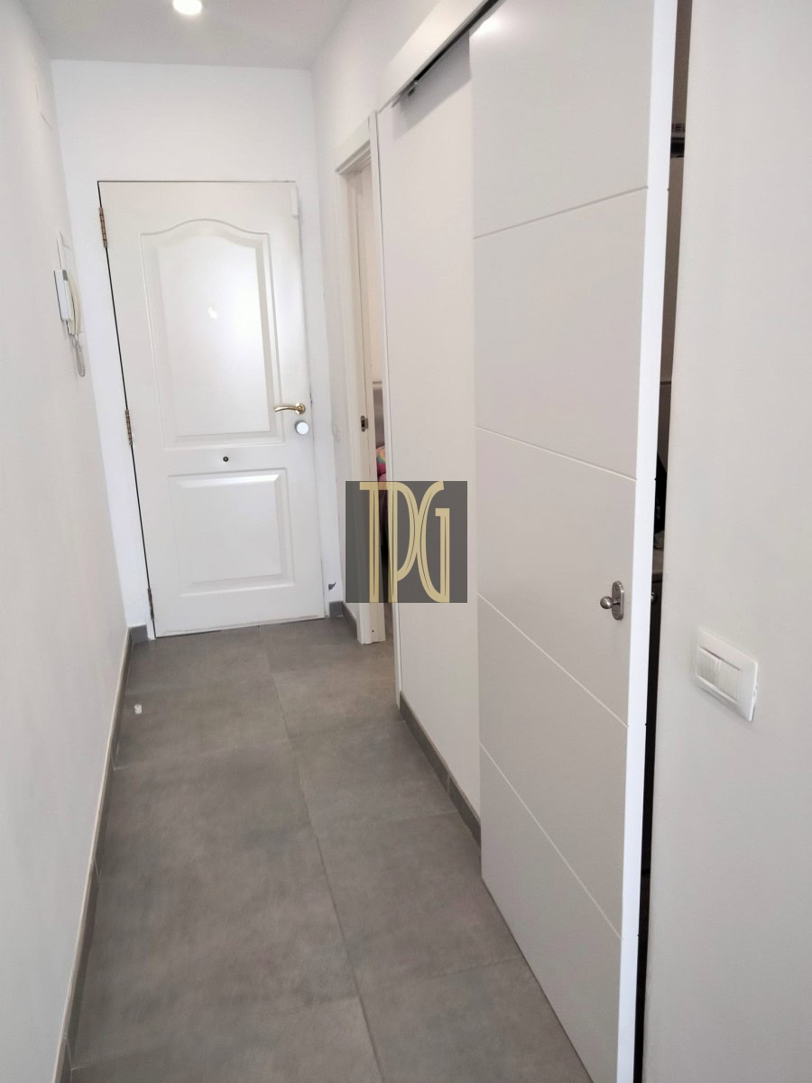 Narrow white hallway with grey tile floor, a closed white front door at the end, and a tall white sliding-door wardrobe on the right.