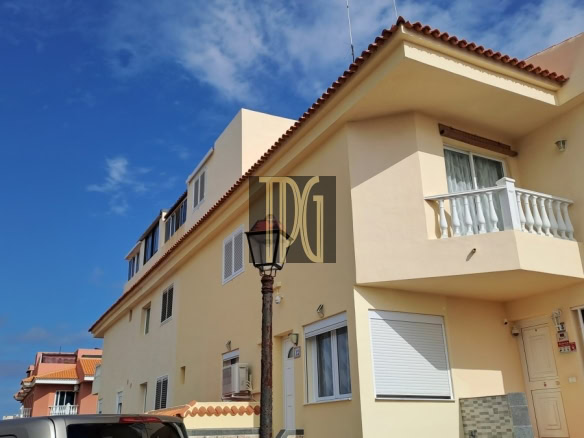Two-story beige house with a small white balcony, under a blue sky, a street lamp in the foreground and a parked car nearby.