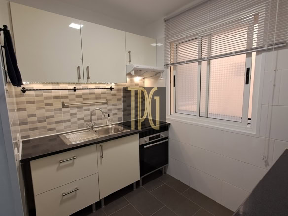 Compact kitchen with white cabinets, tiled backsplash, stainless steel sink, and dark countertop beneath a window with blinds.