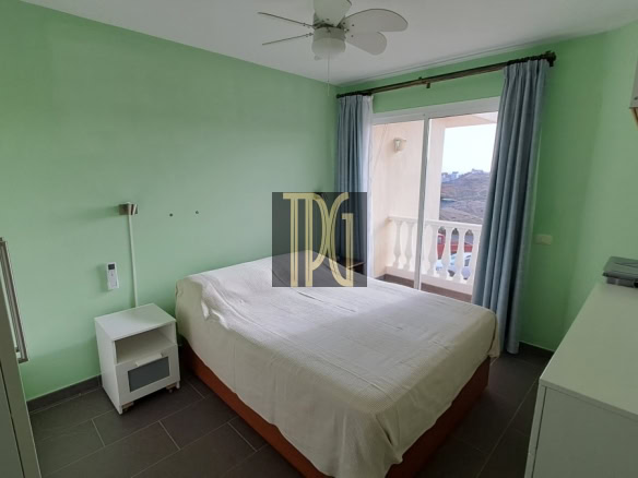 Bedroom with light green walls, a double bed with white bedding, a white nightstand, and a balcony door with blue curtains.