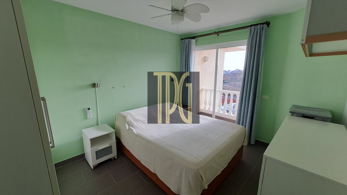 Bedroom with light green walls, a double bed with white bedding, a white nightstand, and a balcony door with blue curtains.