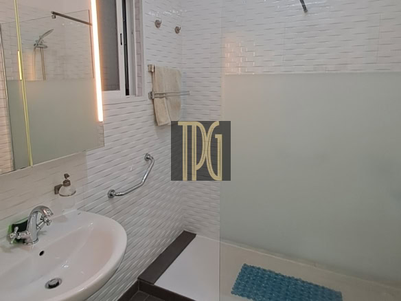 Modern bathroom with a frosted glass shower partition, white tile walls, and a white toilet beside a sink with a curved faucet.