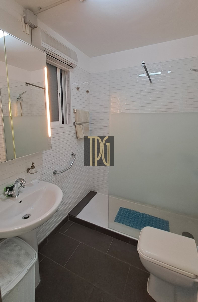 Modern bathroom with a frosted glass shower partition, white tile walls, and a white toilet beside a sink with a curved faucet.