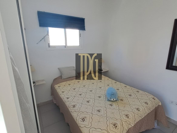 Small bedroom with a double bed covered by a patterned beige bedspread; a blue plush toy sits at the center of the bed.