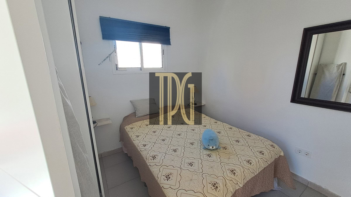 Small bedroom with a double bed covered by a patterned beige bedspread; a blue plush toy sits at the center of the bed.