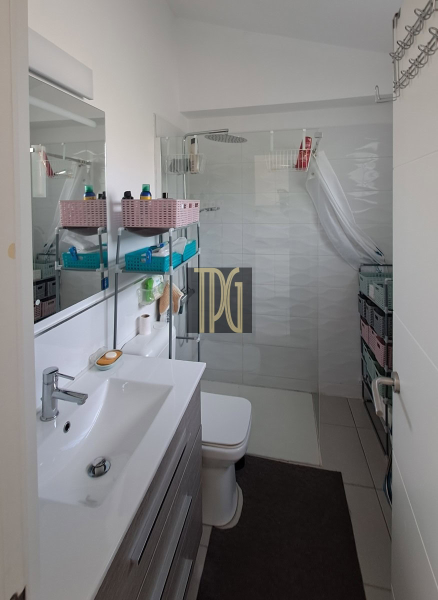 Small modern bathroom with a sink vanity, mirror, toilet, and a glass shower stall with a white curtain. Shelves hold pink baskets and blue organizers, creating organized storage.