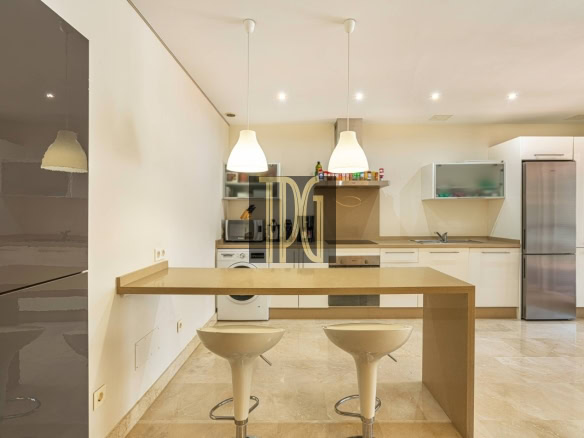 Modern open-plan kitchen with a beige island breakfast bar and two white swivel stools, stainless steel refrigerator, and built-in appliances along the back wall.