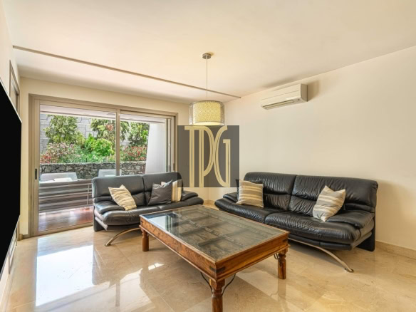 Modern living room with two black leather sofas, a glass-topped wooden coffee table, and sliding doors to a garden.