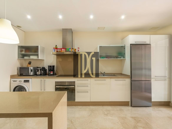 Modern, bright kitchen with white cabinets, a stainless steel fridge, built-in oven, and a beige island in the foreground.