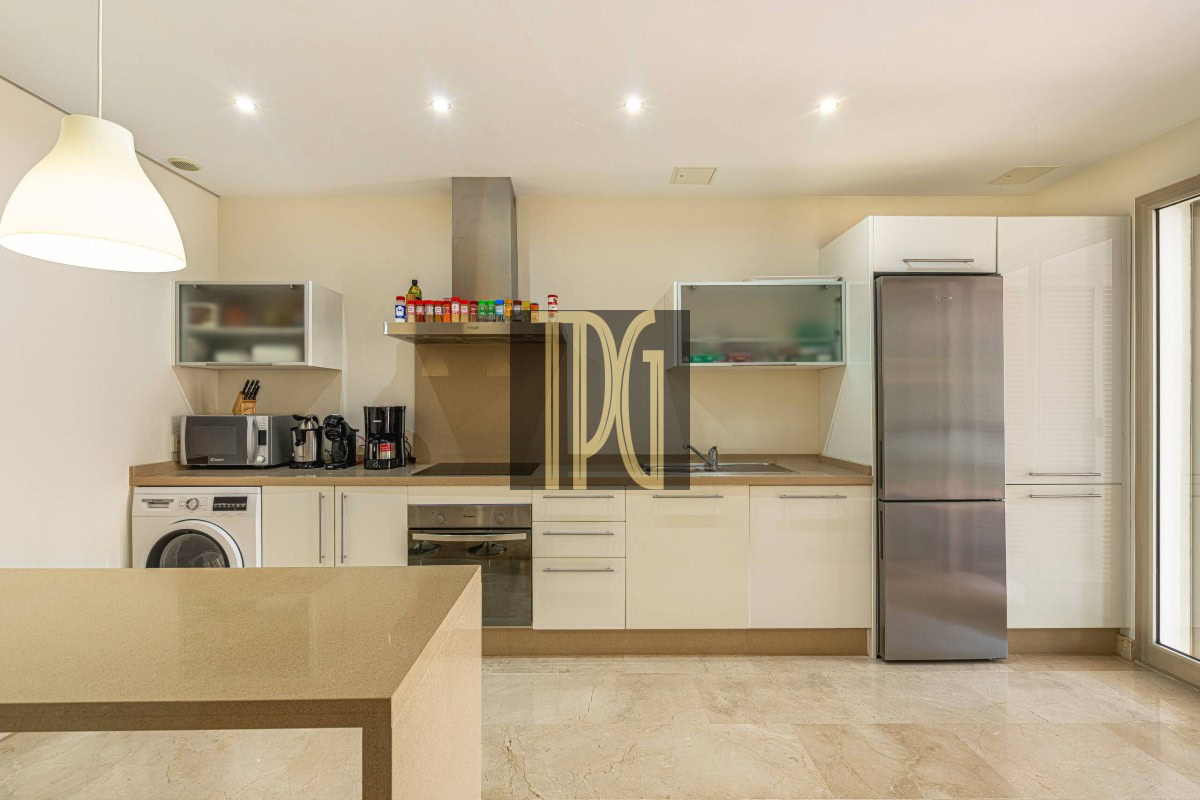 Modern, bright kitchen with white cabinets, a stainless steel fridge, built-in oven, and a beige island in the foreground.
