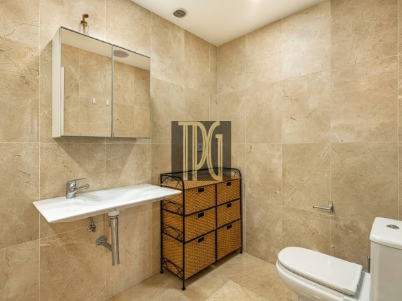 Beige tiled bathroom with a wall-mounted mirror cabinet, white sink, wicker storage drawers, and a toilet beside it.