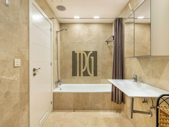 Modern beige-tiled bathroom with a white bathtub, shower head, gray shower curtain, and a white sink with a mirrored cabinet on the right.