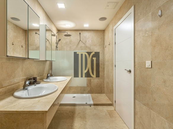 Bathroom with two oval sinks, beige marble countertop, mirrored cabinets, glass shower partition, and a white door in the background.