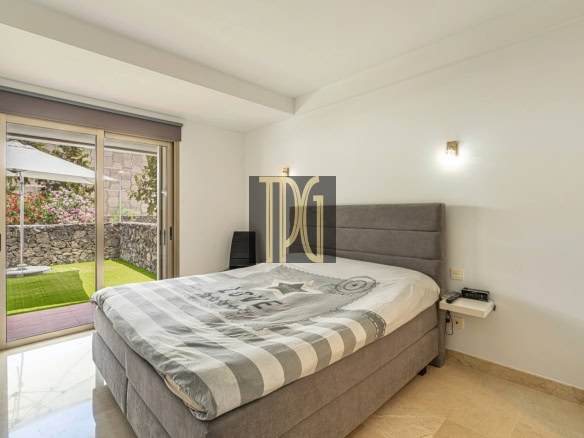 Modern gray upholstered bed in a bright bedroom with a sliding glass door opening to a stone-walled garden.