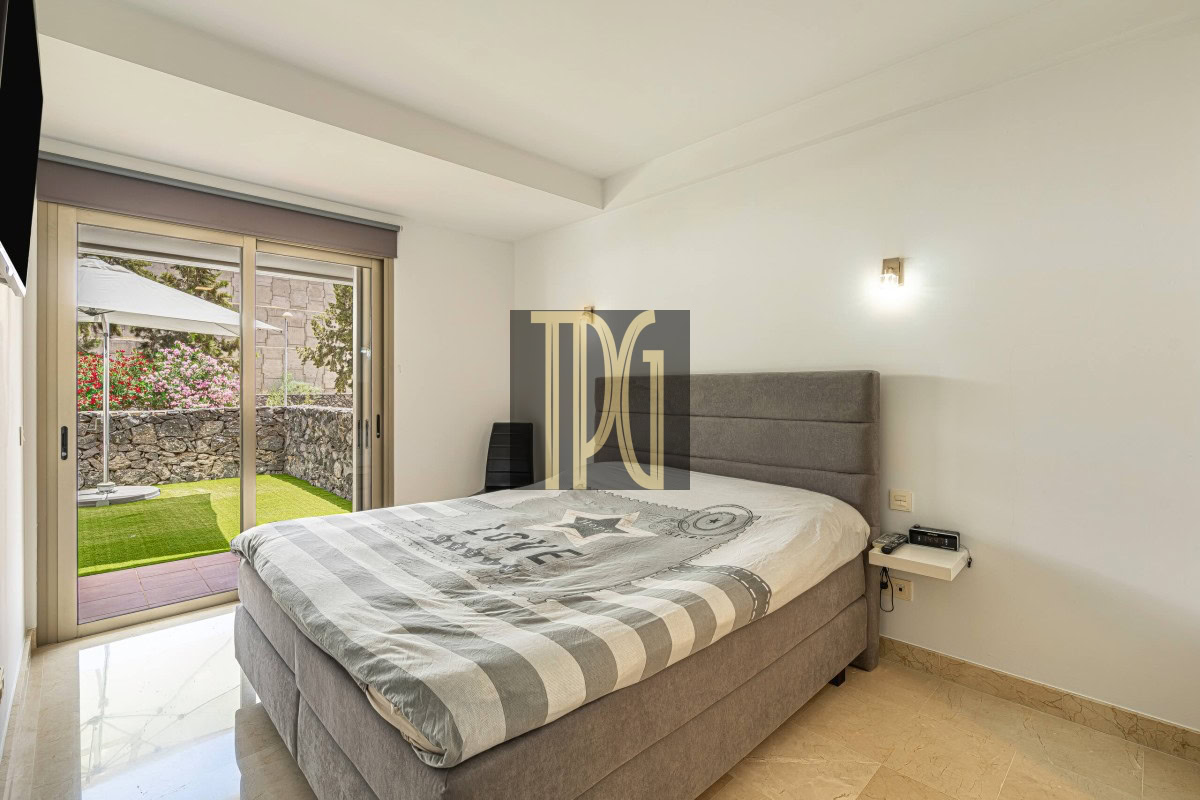 Modern gray upholstered bed in a bright bedroom with a sliding glass door opening to a stone-walled garden.