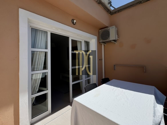 Patio area outside peach-colored walls with white-framed sliding glass doors, an outdoor AC unit, and a table with a white tablecloth and chairs.