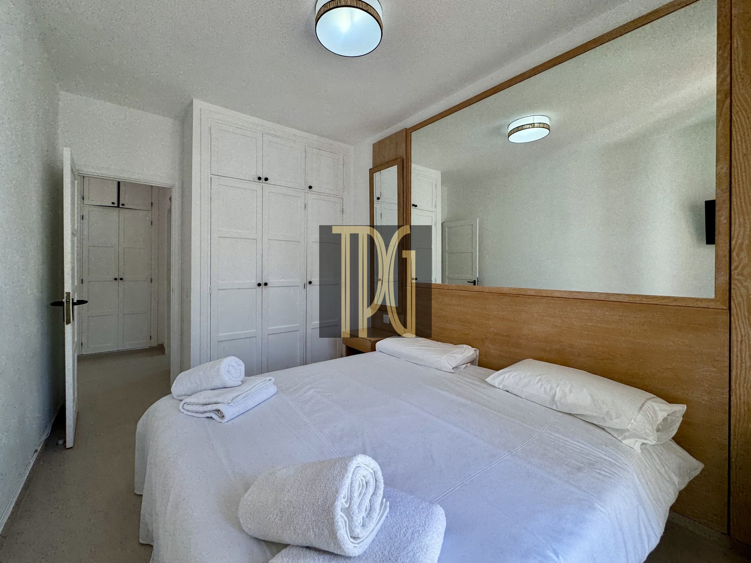 Hotel room with two neatly made beds, rolled towels, and a large wooden-framed mirror reflecting white built-in wardrobes.