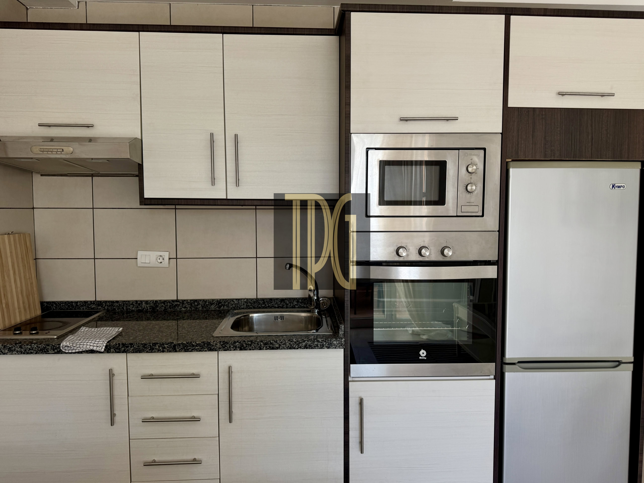 Kitchen with cream cabinets, stainless steel oven and microwave, and a tall refrigerator on the right.
