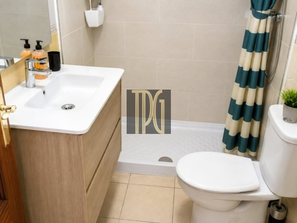 Small modern bathroom with a wooden vanity, white sink, and wall-mounted shower caddies beside a tiled shower area with a teal-striped curtain; toilet nearby.
