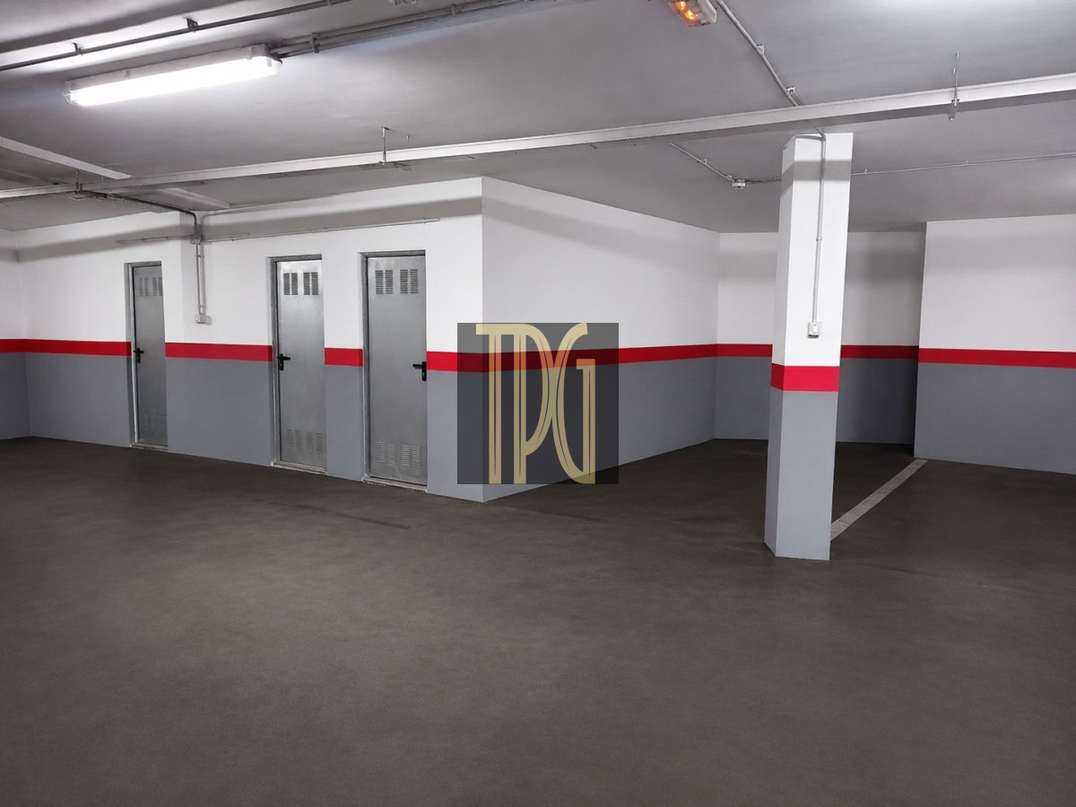 Underground parking area with metal storage doors along a white wall, a red stripe, and a concrete pillar.