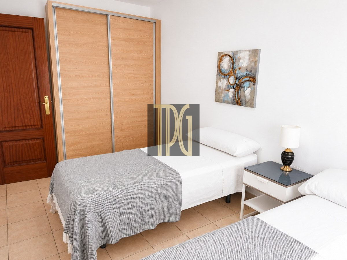 Twin beds in a bright hotel room with a wooden sliding-door wardrobe, a nightstand, and abstract art on the wall.