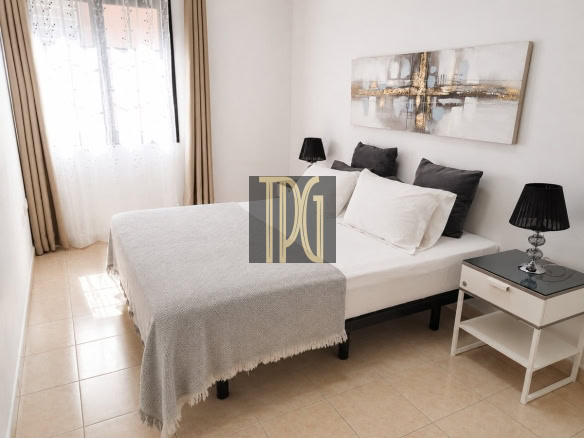 Bright hotel-style bedroom with a white bed, gray pillows, black lamps, and abstract wall art above the headboard.