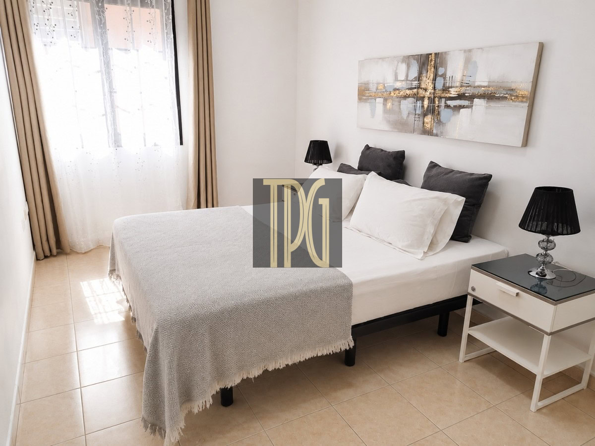 Bright hotel-style bedroom with a white bed, gray pillows, black lamps, and abstract wall art above the headboard.
