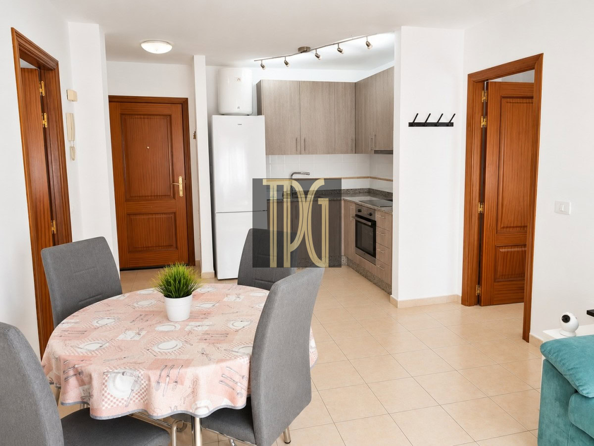 Open-plan dining area with a round table, pink tablecloth, and four gray chairs beside a modern kitchen.