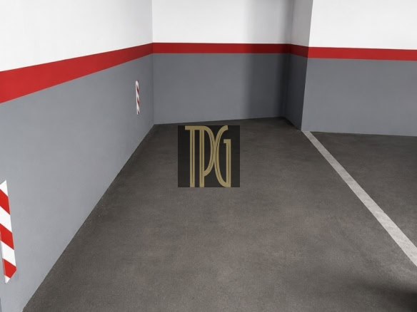 Empty parking space in a concrete garage with white walls above, a red stripe across the middle, and gray lower walls; a white line marks the next spot edges and a black logo sits on the floor.