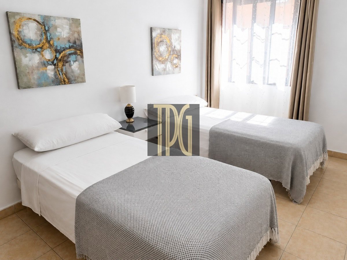 Twin bedroom with two single beds, white linens, gray knit throws, a nightstand and lamp between them.