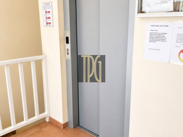 Gray elevator doors in a beige hallway with a small control panel on the left and a notice board on the right.