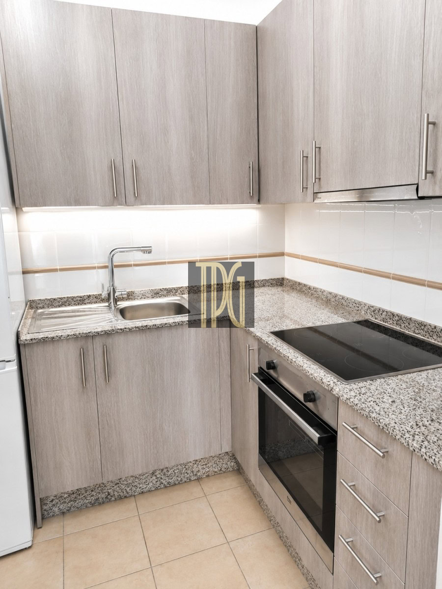 Modern L-shaped kitchen with gray wood cabinets, speckled granite counters, and a stainless sink with faucet.