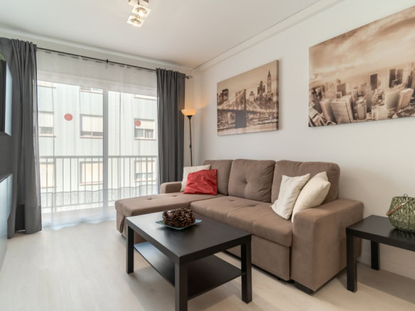 Cozy living room with a tan sofa, white and red cushions, black coffee table, and city skyline art on the wall.