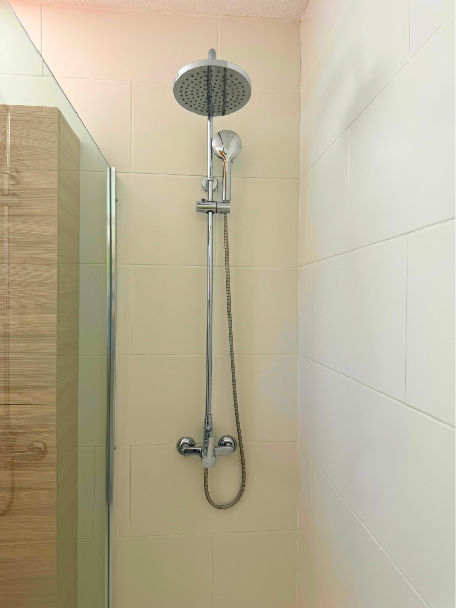 Chrome shower system with a large circular rainfall head and a handheld spray on a tiled bathroom wall