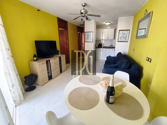Bright living room with yellow walls, TV, and dining area in Tenerife property.