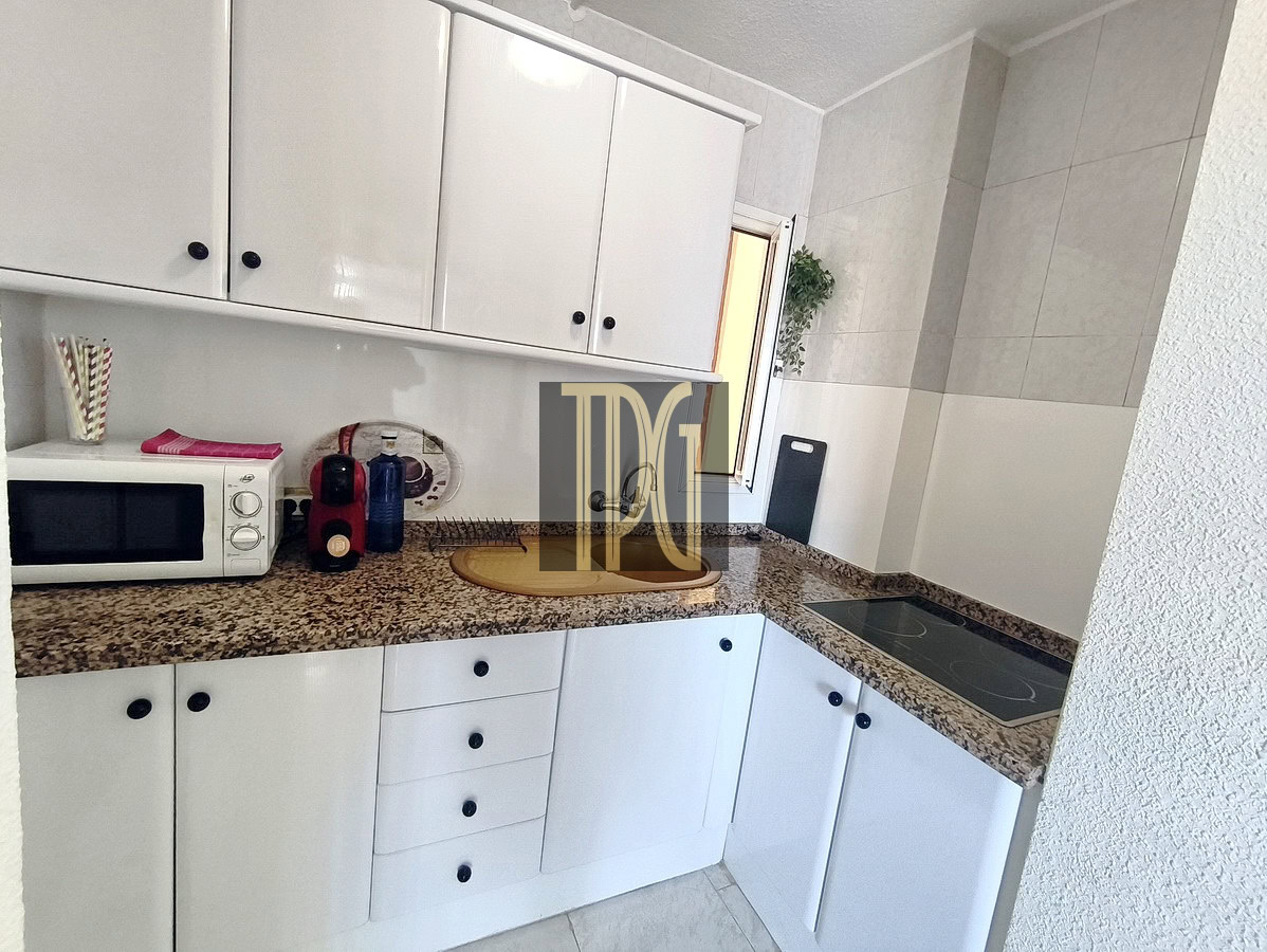 Compact white kitchen with granite counter, microwave, coffee machine, kettle, and induction hob on an L-shaped layout.