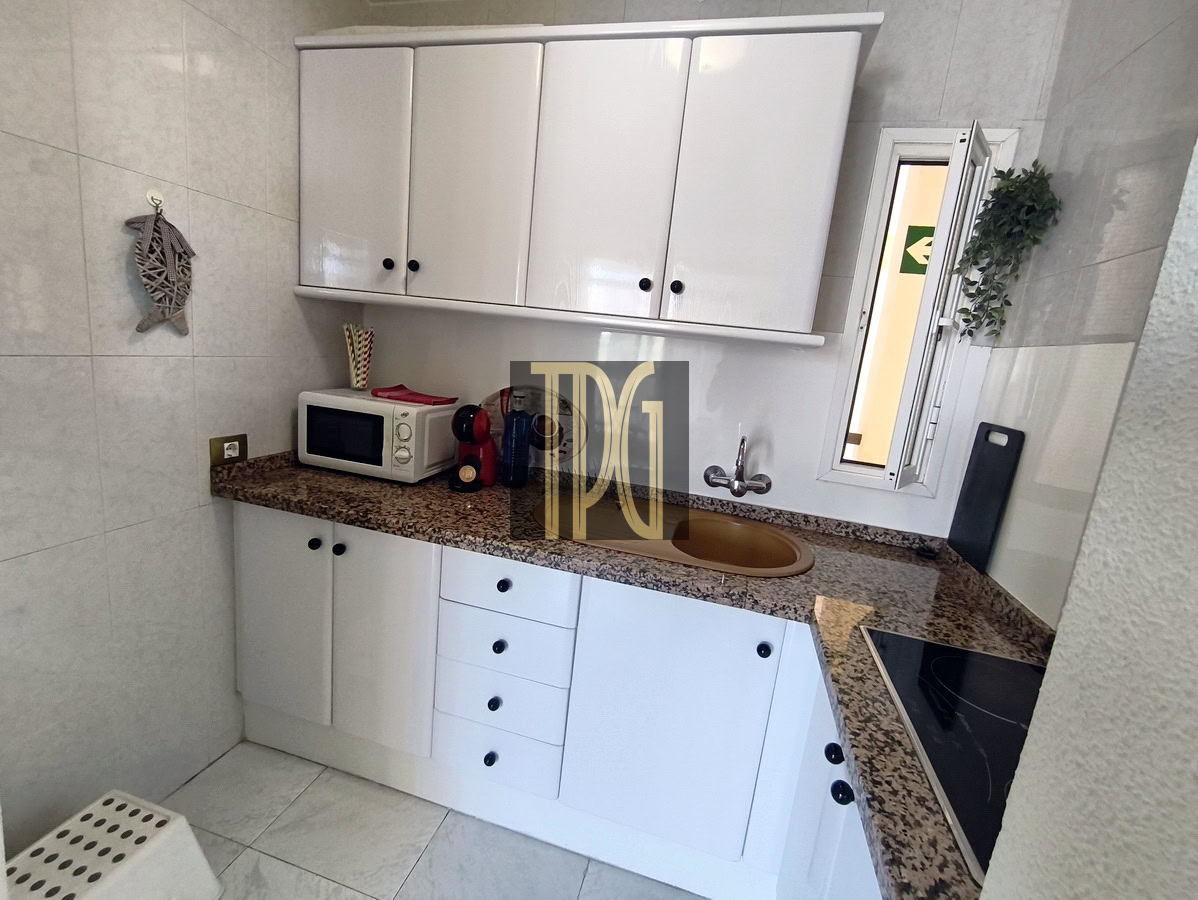 Compact white kitchen with granite countertop, upper and lower cabinets, microwave, coffee maker, and a brown sink.