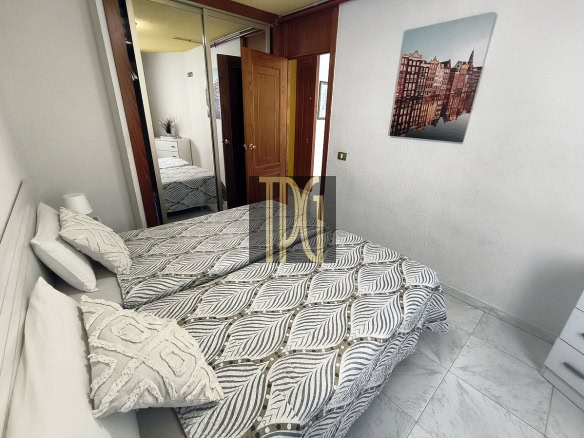 Bedroom with a double bed in patterned gray bedding, white pillows, and a textured throw; mirrored wardrobe, open doors, and a cityscape wall print above the bed.