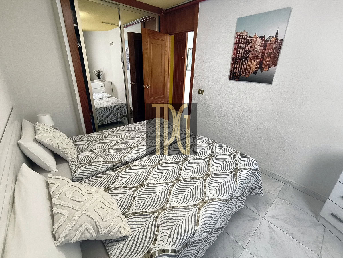 Bedroom with a double bed in patterned gray bedding, white pillows, and a textured throw; mirrored wardrobe, open doors, and a cityscape wall print above the bed.