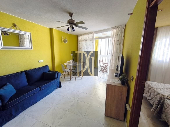 Living room with yellow walls, a blue sofa, a round dining table, and a balcony door with sheer curtains.