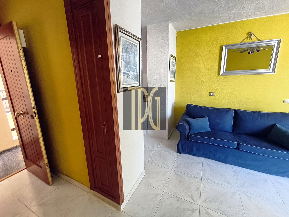 Bright living room with yellow wall, blue sofa, and mirror in Tenerife property.