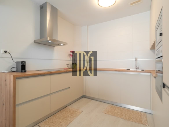 Modern L-shaped kitchen with beige cabinets, wooden countertops, and stainless steel range hood from above. (informative)
