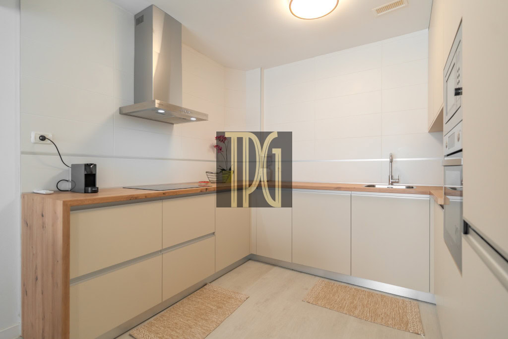 Modern L-shaped kitchen with beige cabinets, wooden countertops, and stainless steel range hood from above. (informative)