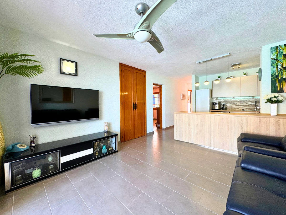 Open-concept living room with a wall-mounted TV above a black glass-front cabinet and a wooden double door in the back corner.