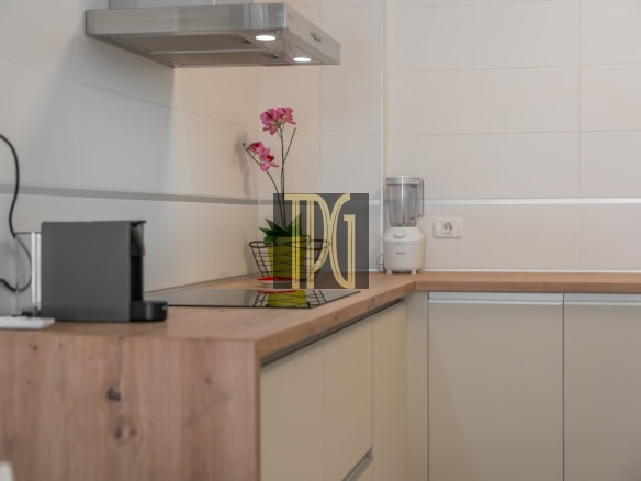Modern kitchen counter with a coffee machine on the left, a blender on the right, and a pink orchid in a vase near the center