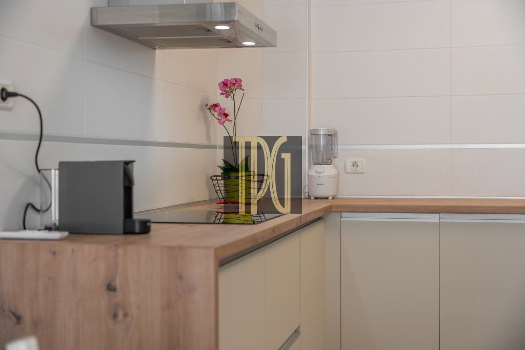 Modern kitchen counter with a coffee machine on the left, a blender on the right, and a pink orchid in a vase near the center