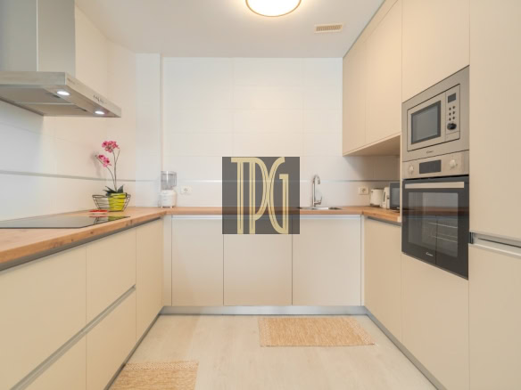 Modern U-shaped kitchen with light beige cabinets, wooden countertops, and built-in stainless steel oven and microwave on the right wall