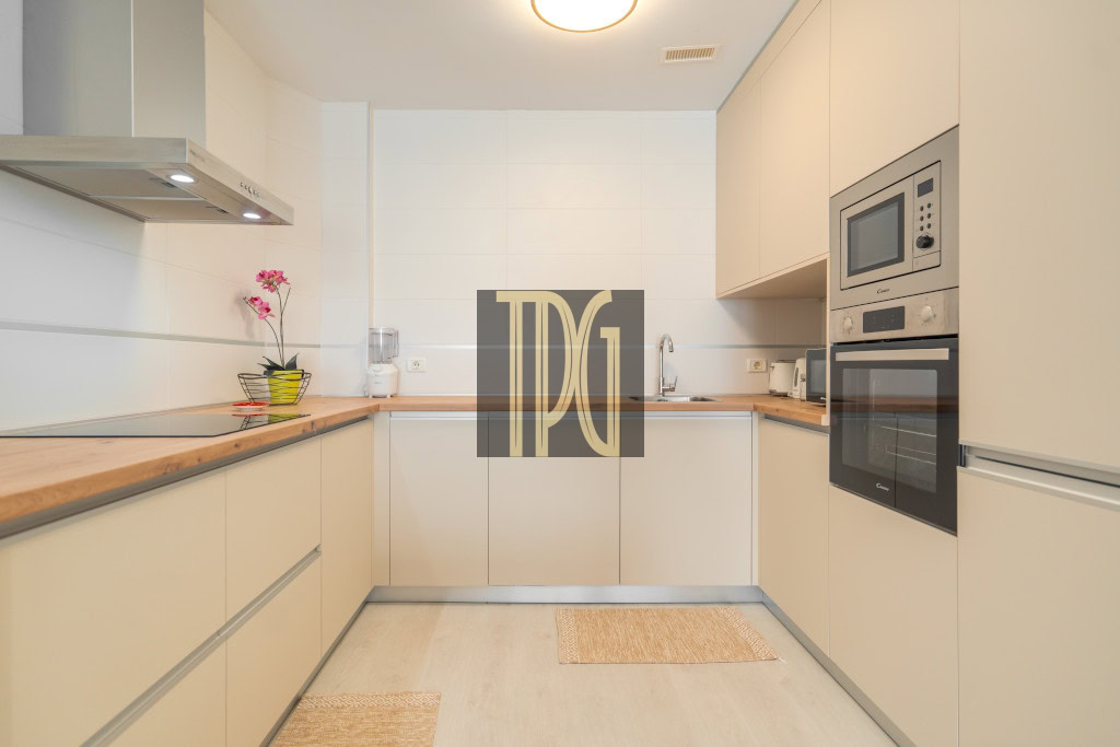 Modern U-shaped kitchen with light beige cabinets, wooden countertops, and built-in stainless steel oven and microwave on the right wall