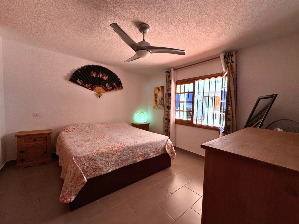 Bedroom with a queen bed, floral quilt, two wooden nightstands, and a ceiling fan above.