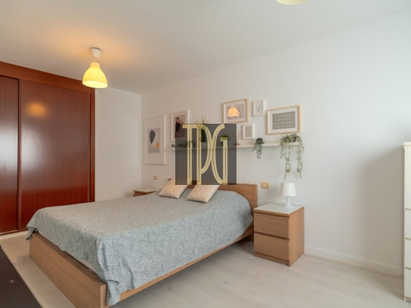 Cozy modern bedroom with a wooden bed frame, grey patterned duvet, two nightstands, and a gallery wall of framed art and plants.